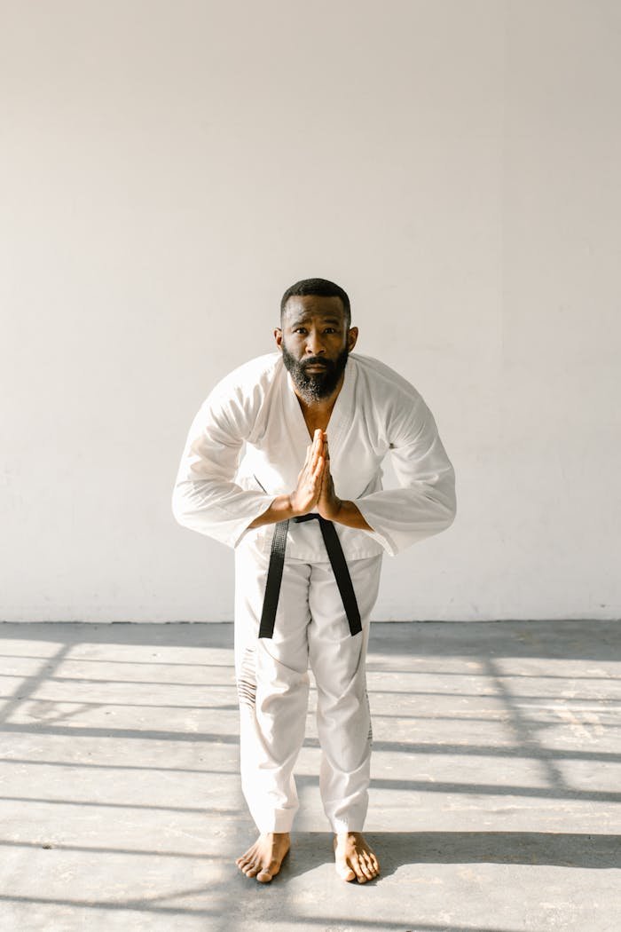 A bearded man in karate gi bowing respectfully in a sunlit room.