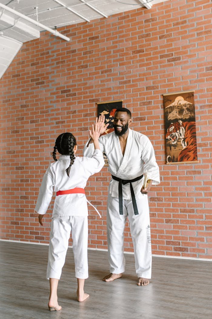 Martial arts instructor and child student high-five during training in indoor studio.