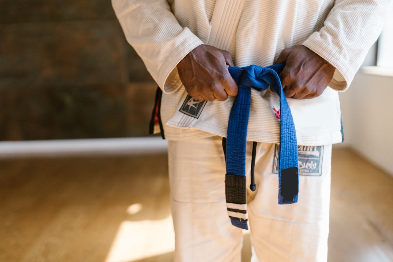 Martial artist in white gi adjusting blue belt with focus on technique and discipline.